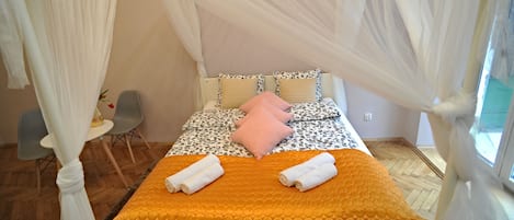 A bed with a canopy, a small table with a vase, and a chair.
