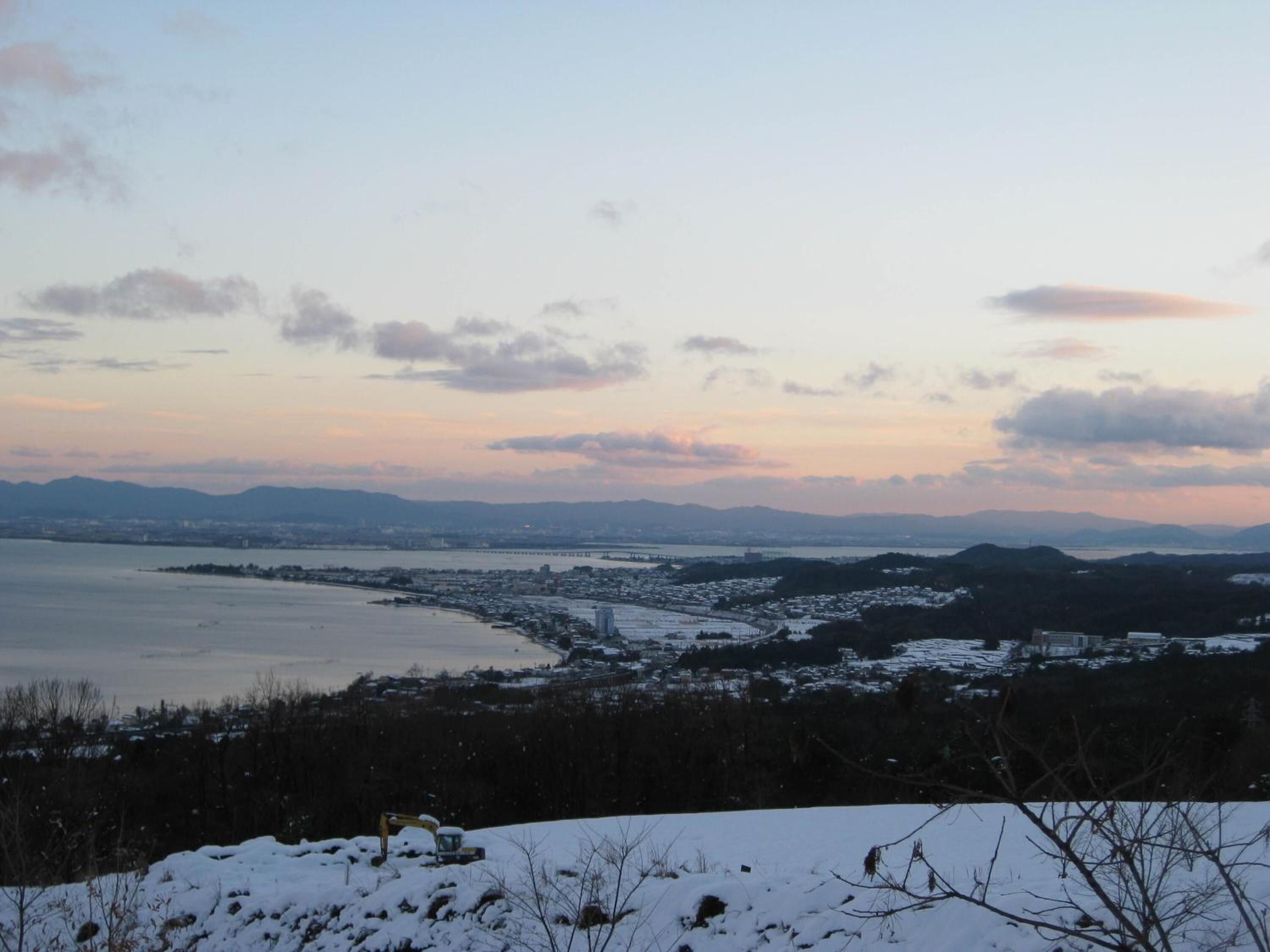 A panoramic view of a coastal city with snow-covered hills and a distant mountain range.