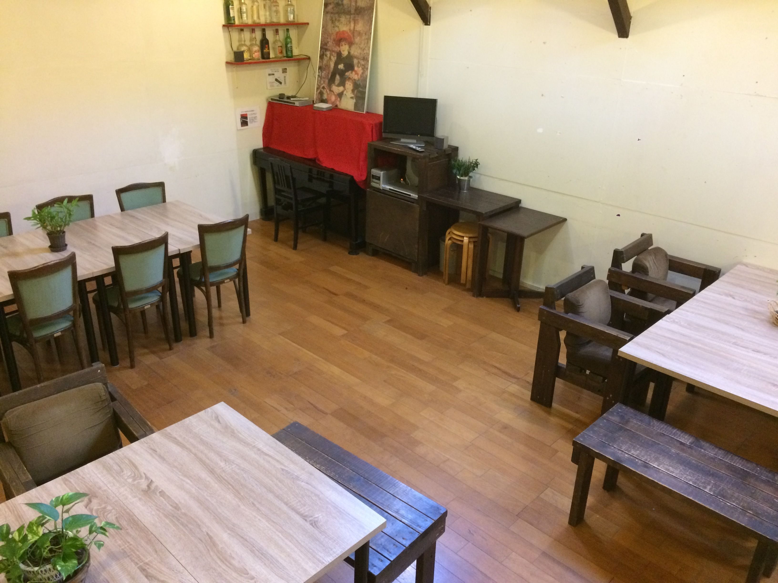 Un comedor con mesas y sillas de madera, una mesa cubierta con mantel rojo y un televisor sobre un soporte.