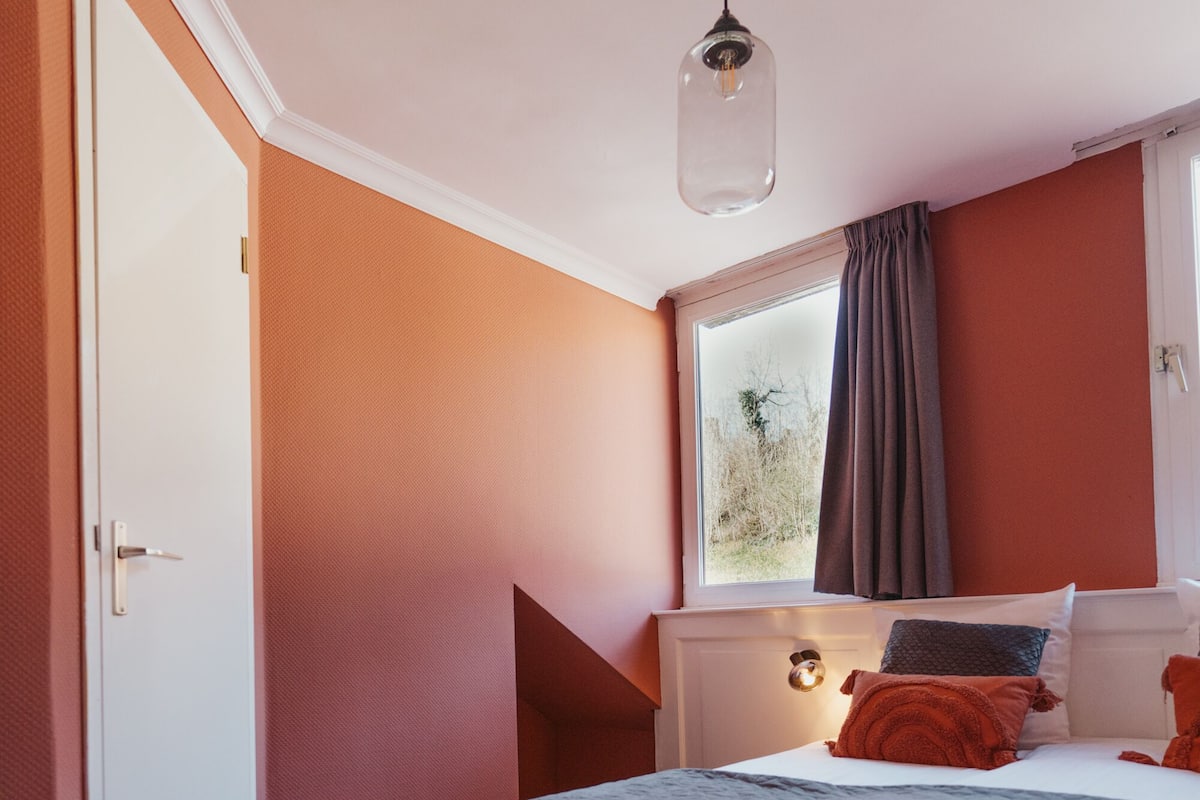 Une chambre à coucher avec un lit, une fenêtre avec des rideaux, une porte et un luminaire.