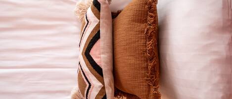 A bed with white linens and two decorative pillows, one striped and one solid brown.