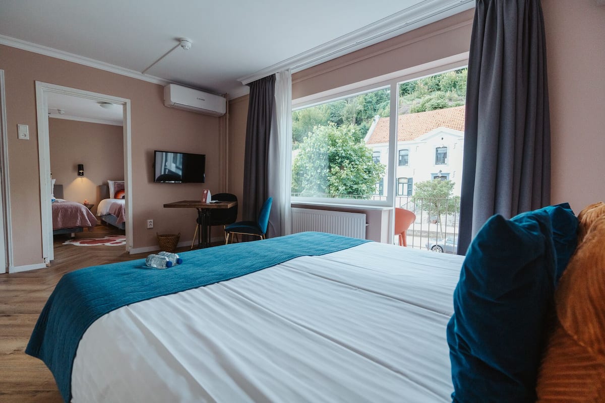 Une chambre d’hôtel avec un grand lit, un bureau, une chaise, une télévision et une fenêtre donnant sur des immeubles et des arbres.