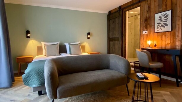 A modern bedroom with a curved sofa, a small round table, and a bed with two pillows. - Hotel Janssen (Valkenburg aan de Geul)