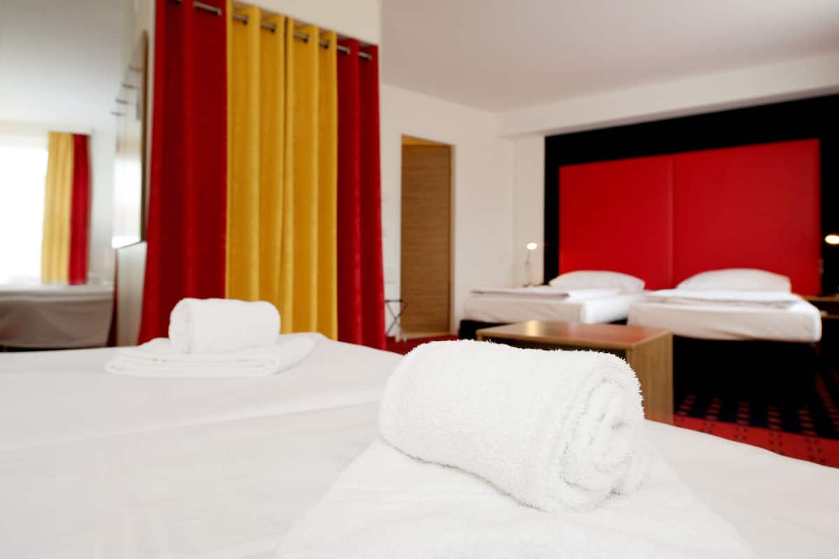 A hotel room with a neatly made bed, a bedside table, and a red accent wall.