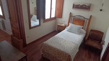 A bedroom with a bed, a nightstand, a chair, a wooden table, a mirror, and a window.