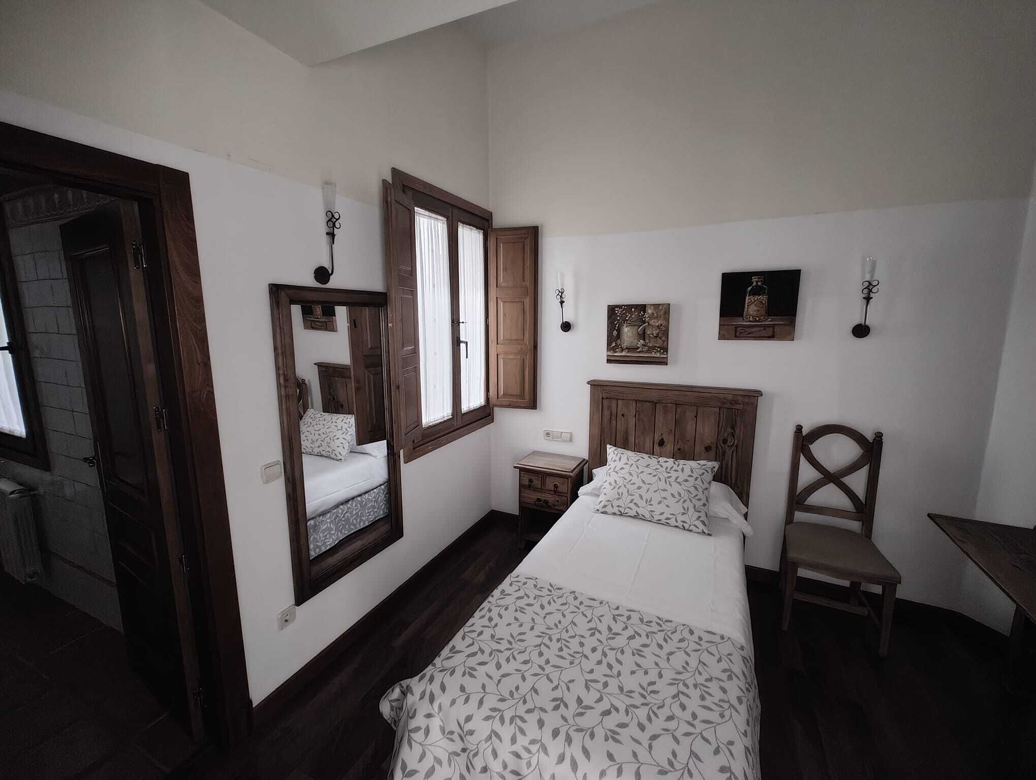 A bedroom with a bed, a chair, a nightstand, a mirror, and a window.