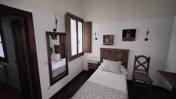 A bedroom with a bed, a chair, a nightstand, a mirror, and a window.