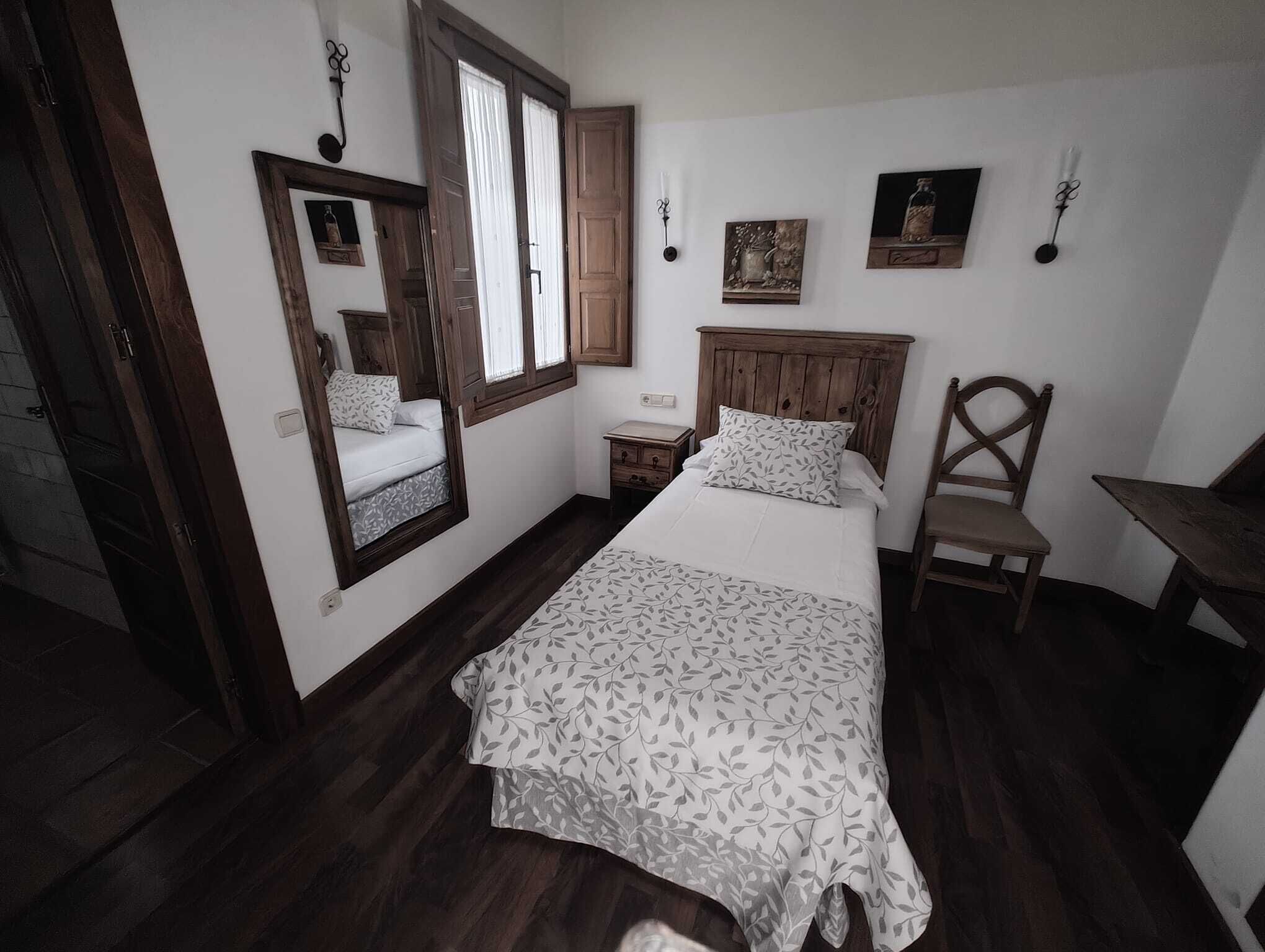 Um quarto com cama, cadeira, mesa de cabeceira e janela com cortinas.