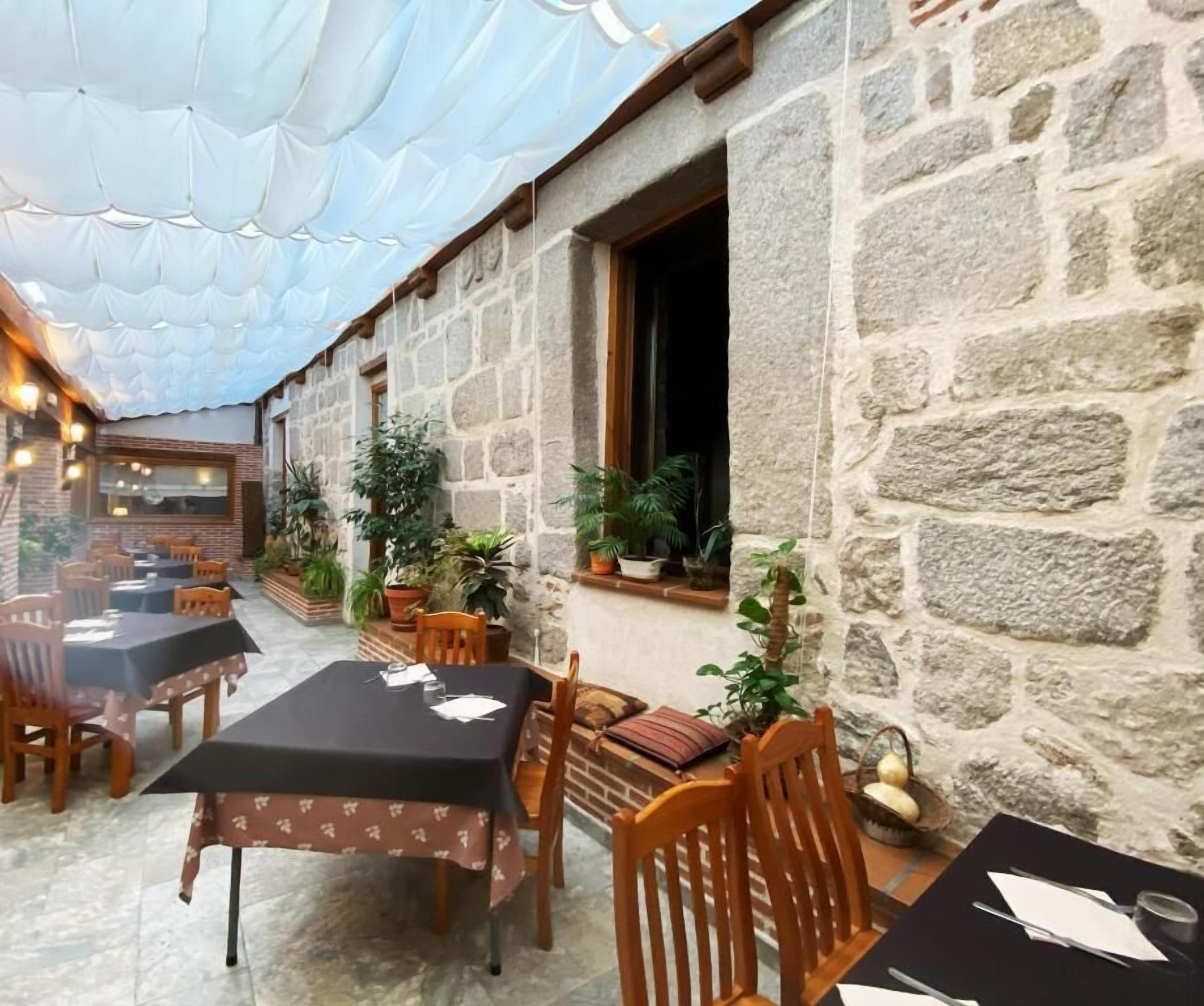 Un espace de restauration en plein air avec des murs en pierre, des tables recouvertes de nappes noires, des chaises en bois et des plantes en pot.