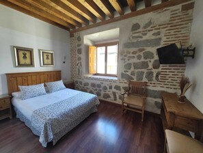A bedroom with a wooden bed, a stone wall, a window, and a chair.