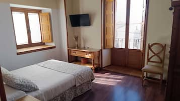 Un dormitorio con cama, escritorio, silla, televisor y puerta al balcón.