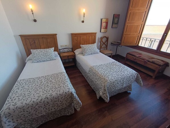 Una habitación con dos camas de madera, una mesita, una silla y un banco.