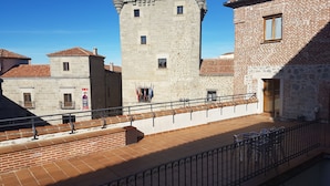 Un patio con una torre de piedra, un edificio de tejado a la vista y una barandilla de metal.
