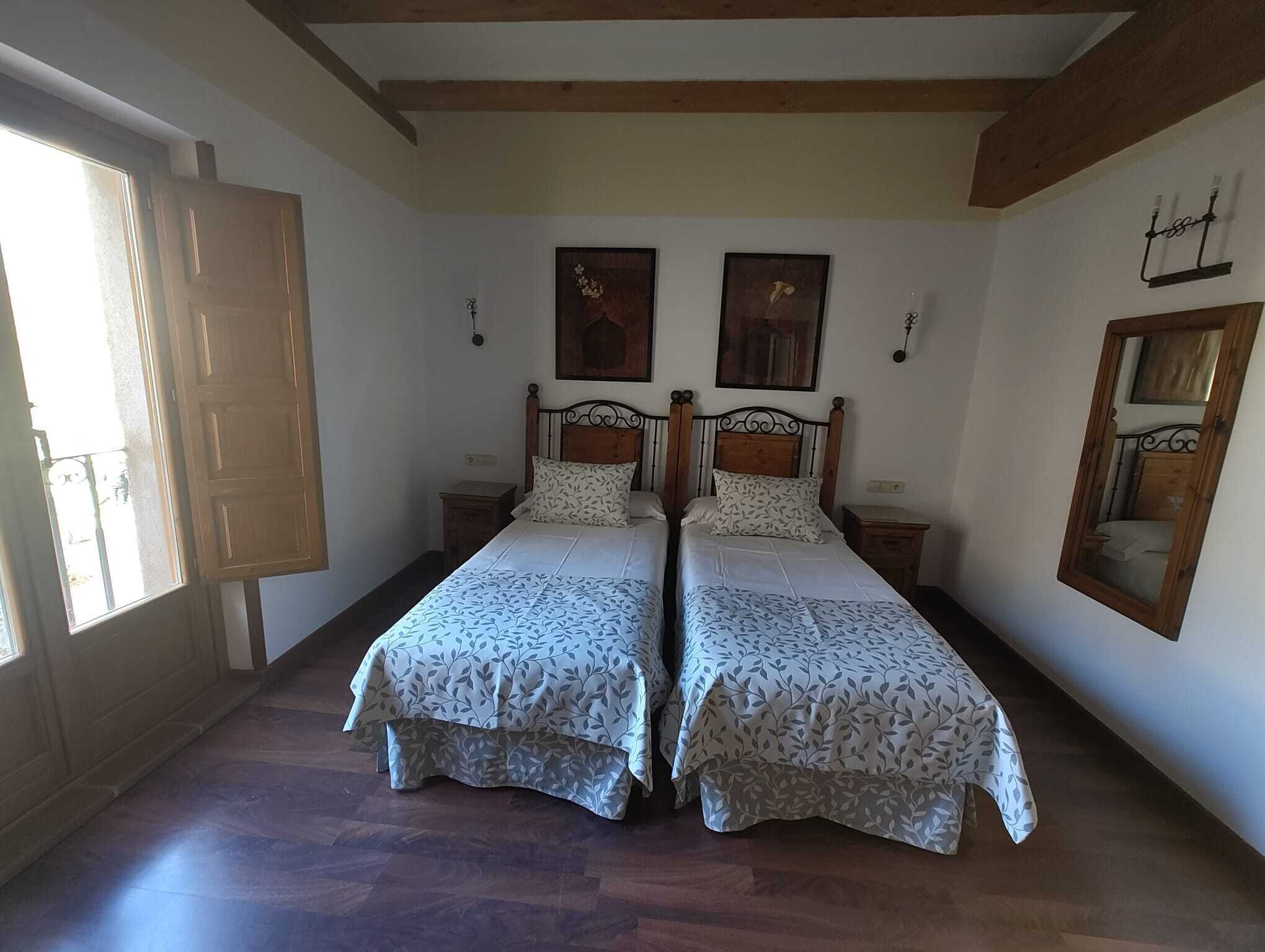 Una habitación con dos camas, vigas de madera en el techo, un ventanal con puerta de madera y obras de arte colgadas en la pared.
