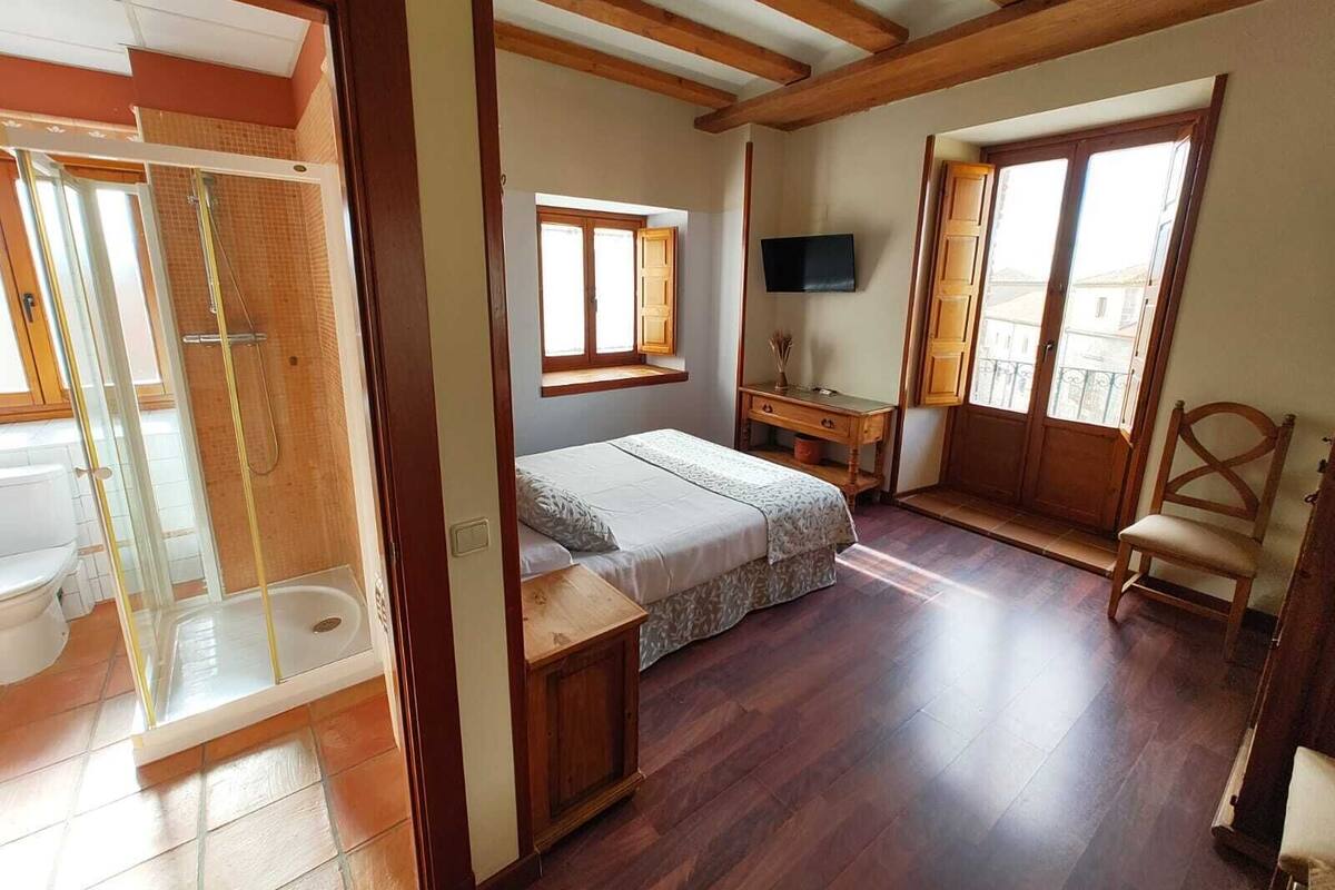 A bedroom with a bed, a desk, a TV, a chair, and a bathroom with a shower.