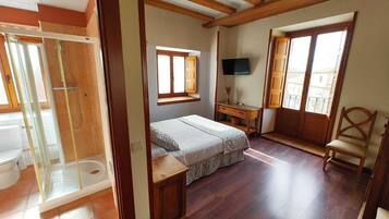 Een slaapkamer met een bed, een bureau, een televisie, een stoel en een badkamer met douche.
