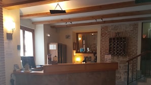 Una zona de recepción con un mostrador de madera, una computadora y una estantería de vinos en la pared.