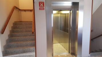 A staircase leading to an elevator with a red safety sign on the wall.