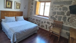 Un dormitorio con cama de madera, paredes de piedra, chimenea de piedra y una ventana.