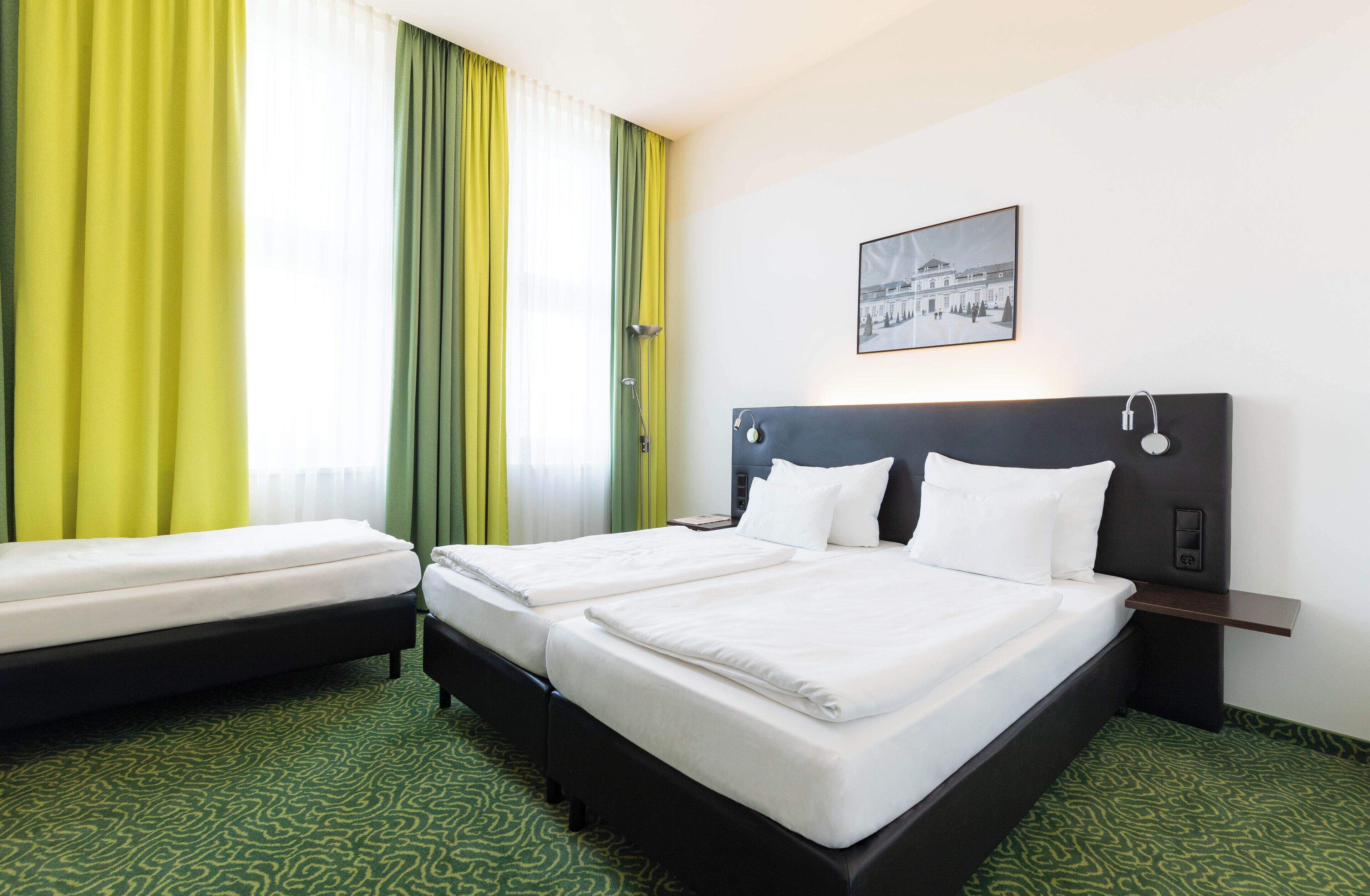 A hotel room with two beds, a headboard with a control panel, a bedside table, and a window with curtains.
