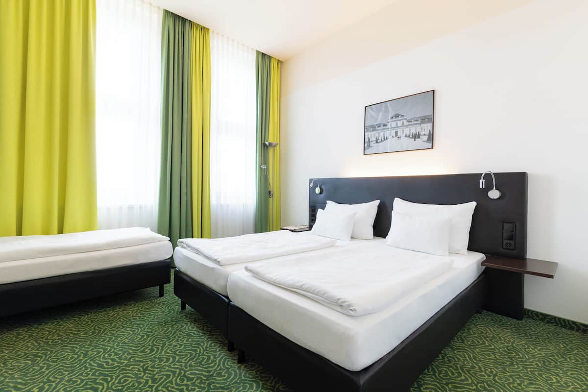 Ein Hotelzimmer mit zwei Betten, einem Kopfteil mit Bedienfeld, einem Nachttisch und einem Fenster mit Vorhängen.