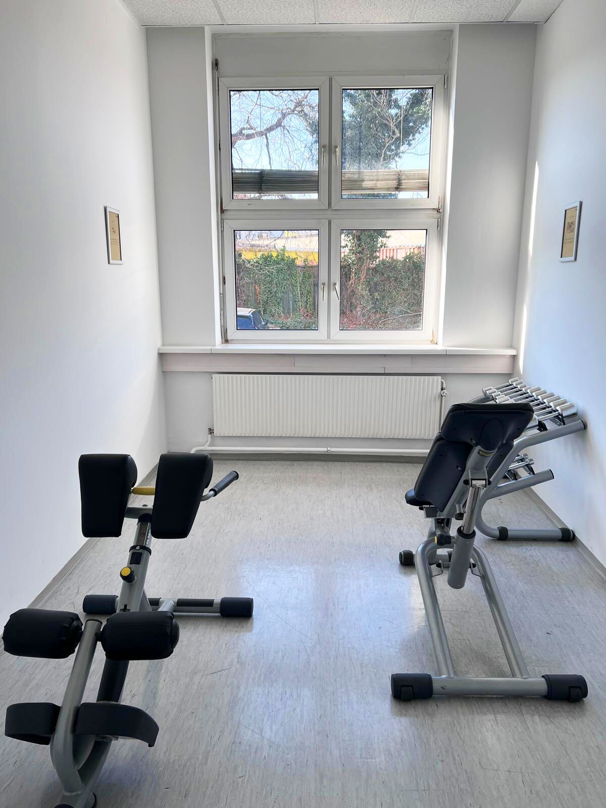 Un gimnasio con dos máquinas de ejercicio, un ventanal con persianas y un radiador.