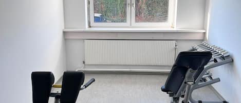 Un gimnasio con dos máquinas de ejercicio, un ventanal con persianas y un radiador.