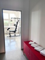Uma academia com equipamentos de exercício, um banco e um armário vermelho com toalhas.