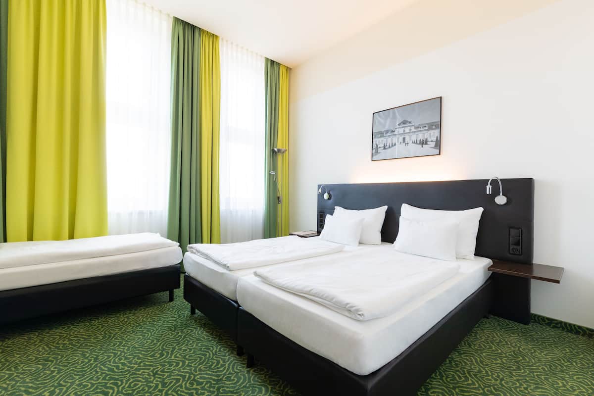 A hotel room with two beds, a nightstand, a wall-mounted clock, and a framed picture.