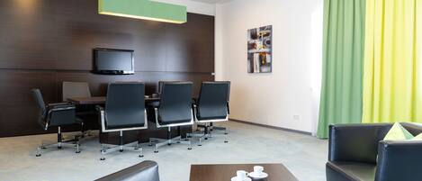 A modern meeting room with a flat-screen TV, conference table, and black chairs.