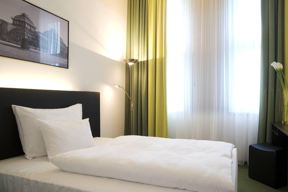 A hotel room with a bed, a nightstand, a lamp, a picture on the wall, and curtains.