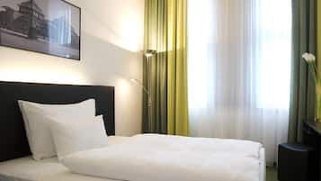 Een hotelkamer met een bed, nachtkastje, lamp, foto aan de muur en gordijnen.