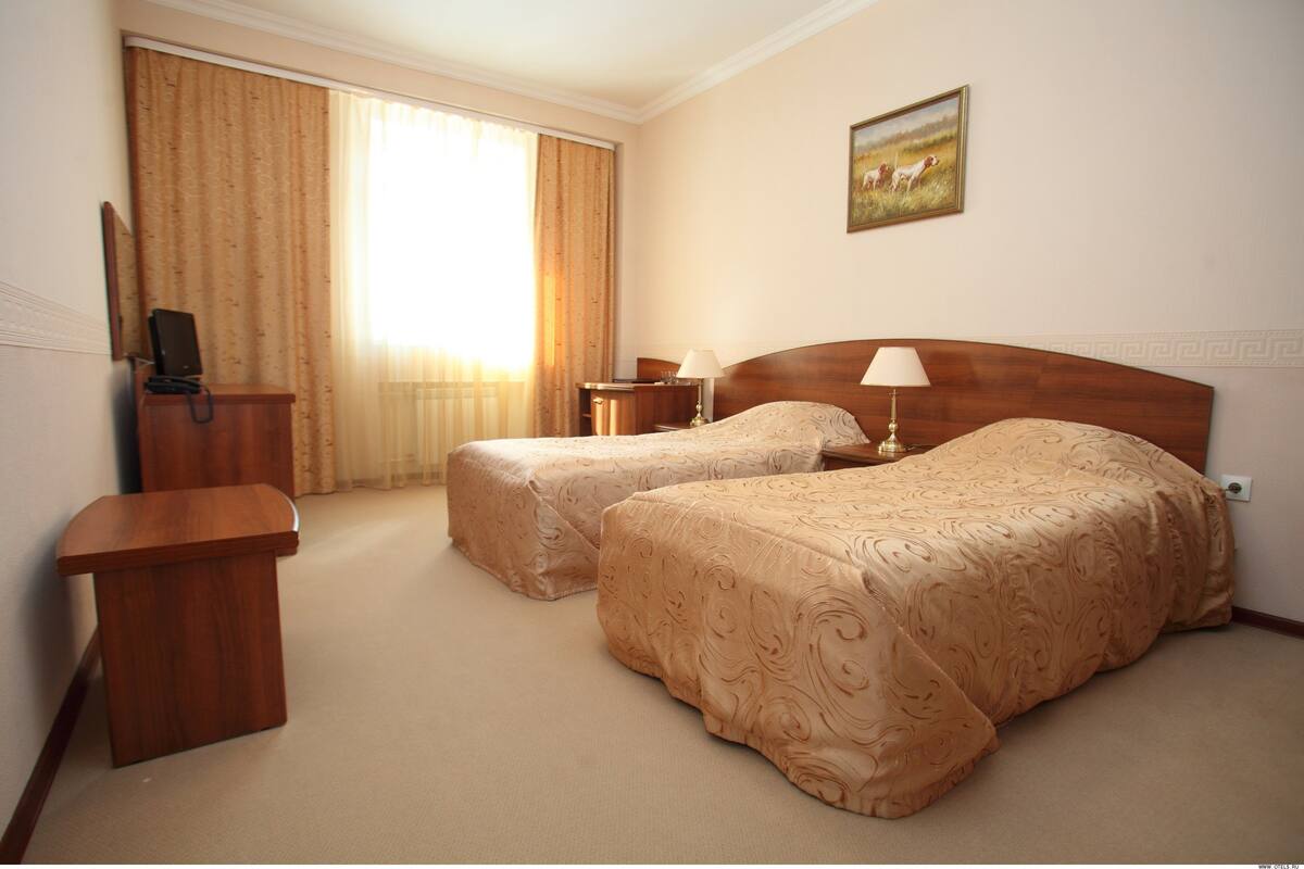 Ein Hotelzimmer mit zwei Betten, einem Schreibtisch, einem Stuhl, einer Lampe und einem Bild an der Wand.