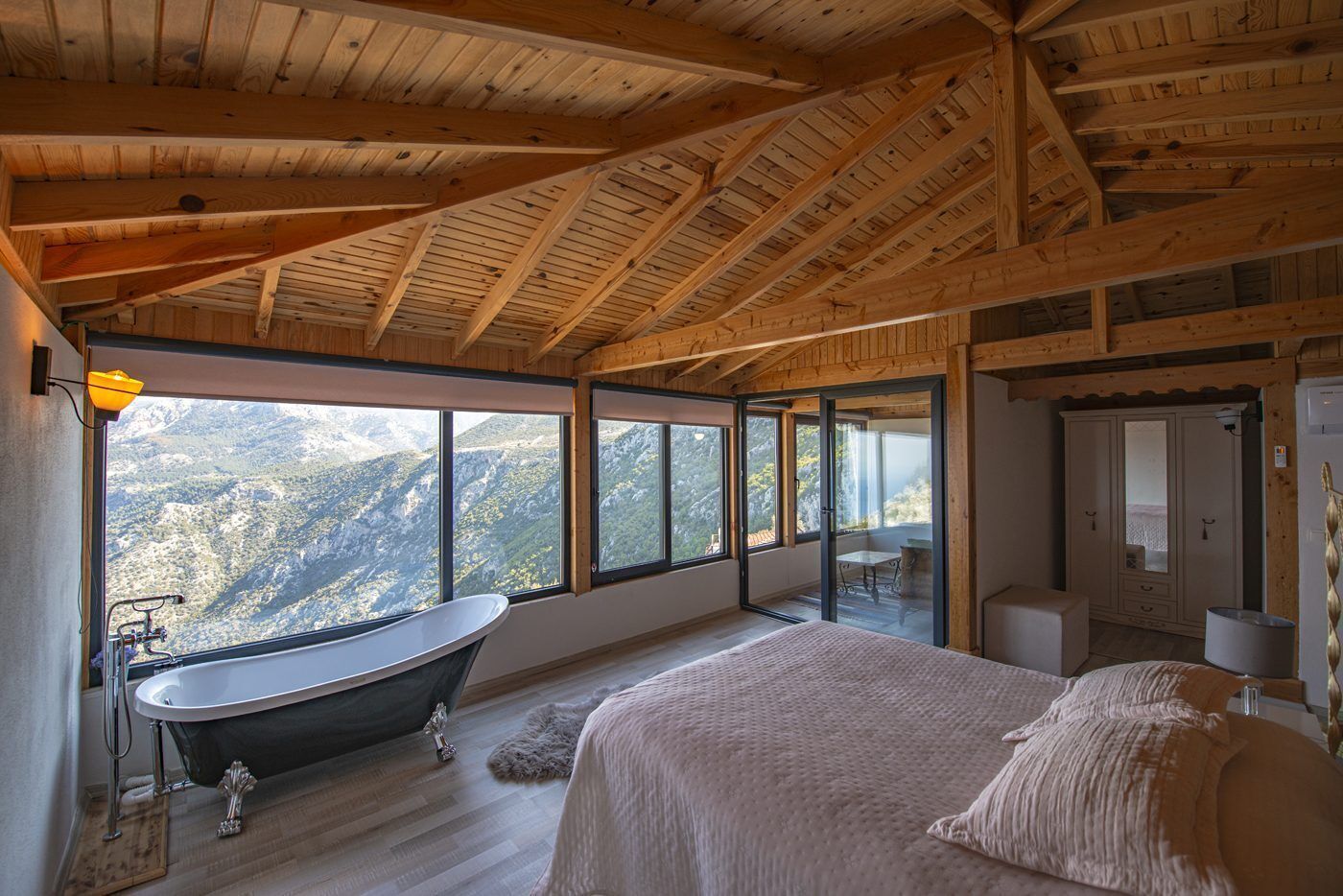 A bedroom with a large bed, a bathtub, and a view of mountains through large windows.