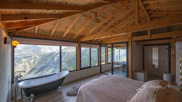 A bedroom with a large bed, a bathtub, and a view of mountains through large windows.