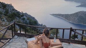 Mulher sentada em uma espreguiçadeira apreciando a vista panorâmica da água e das colinas.