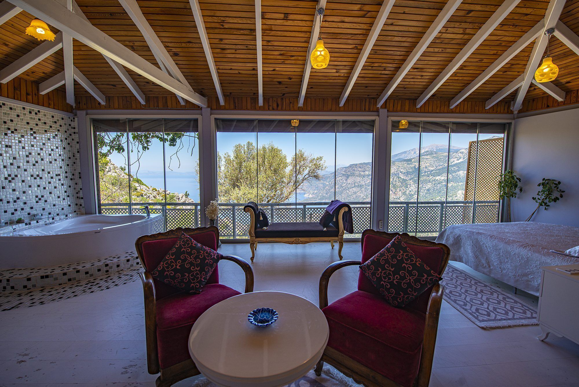 Una habitación con techo de madera, ventanas amplias, un sofá, dos sillones y una pequeña mesa.