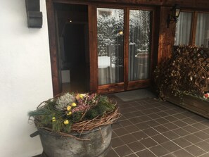 A wooden door with glass panels, a potted plant with greenery and yellow ornaments, and a tiled floor. - Alpenchalet Monika (Ried im Zillertal)