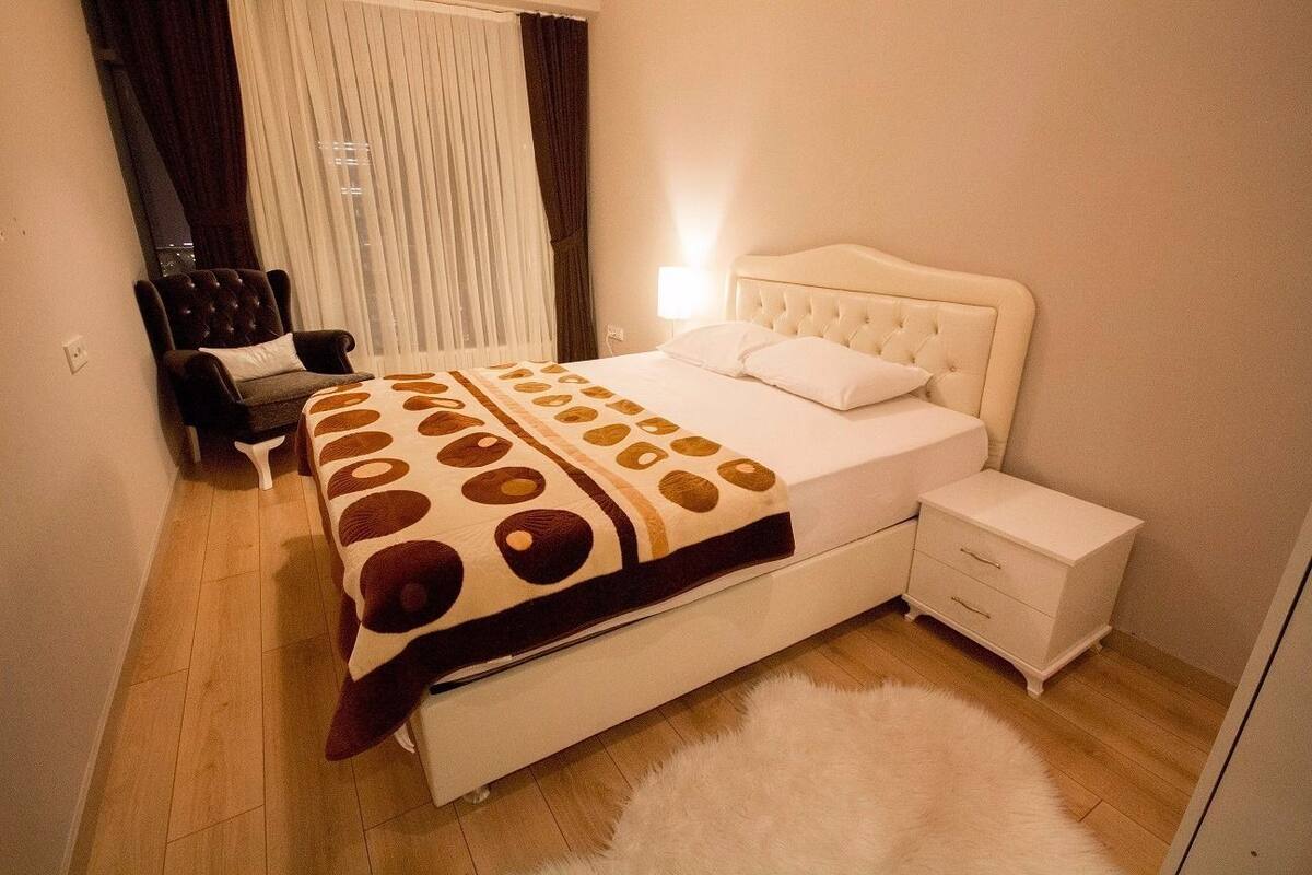 A bedroom with a bed, a chair, a nightstand, and a window with curtains.