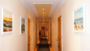 A hotel hallway with framed pictures on the walls, wooden doors, and a carpeted floor. - Haus Am Wald (Heringsdorf)