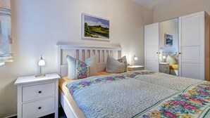A bedroom with a bed, nightstands, a dresser, and a painting on the wall. - Haus Am Wald (Heringsdorf)