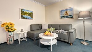 A modern living room with a grey sofa, a round white coffee table, a vase with sunflowers, and two paintings on the walls. - Haus Am Wald (Heringsdorf)