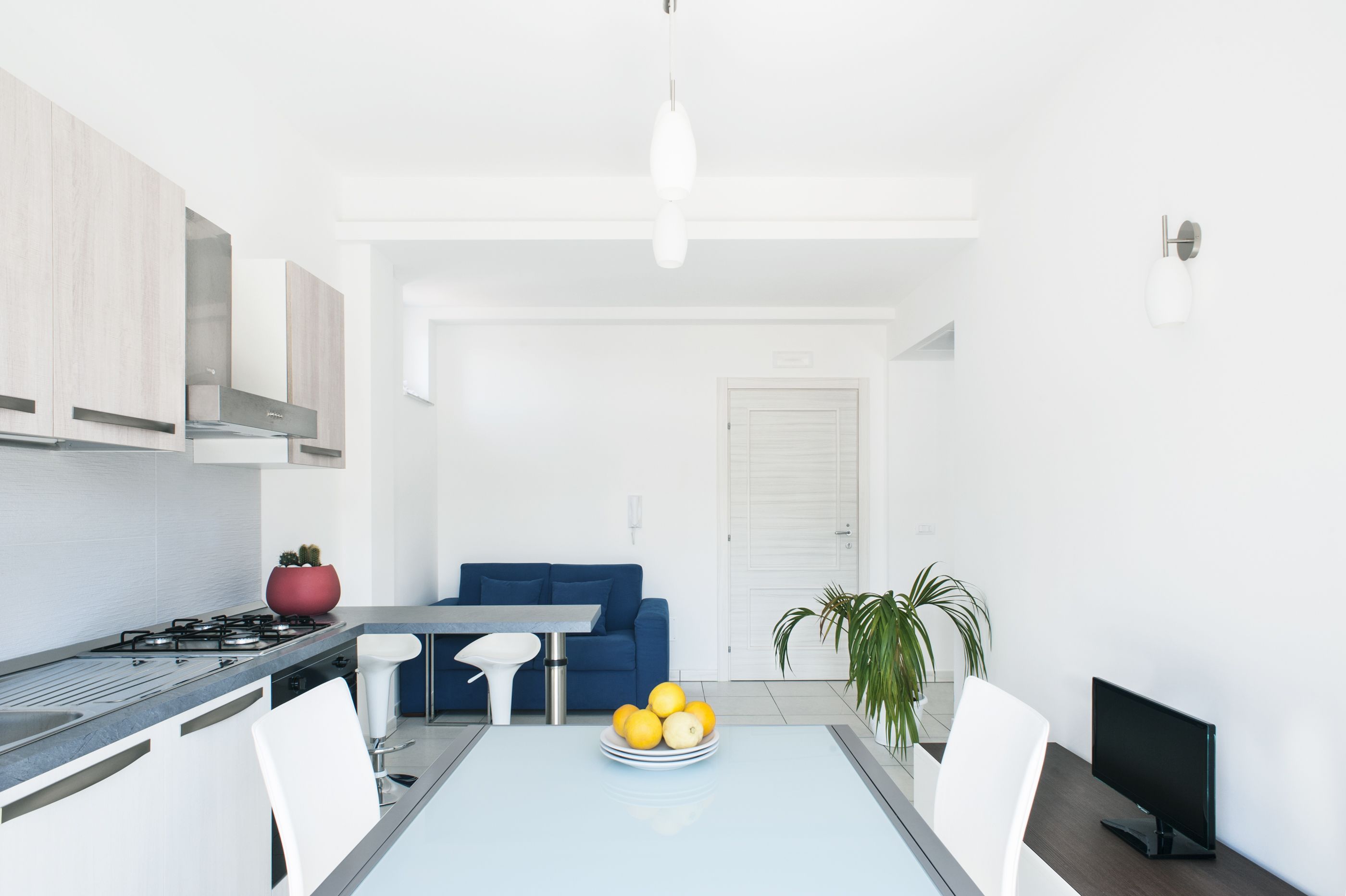 A modern kitchen with a dining area, a blue sofa, and a TV.