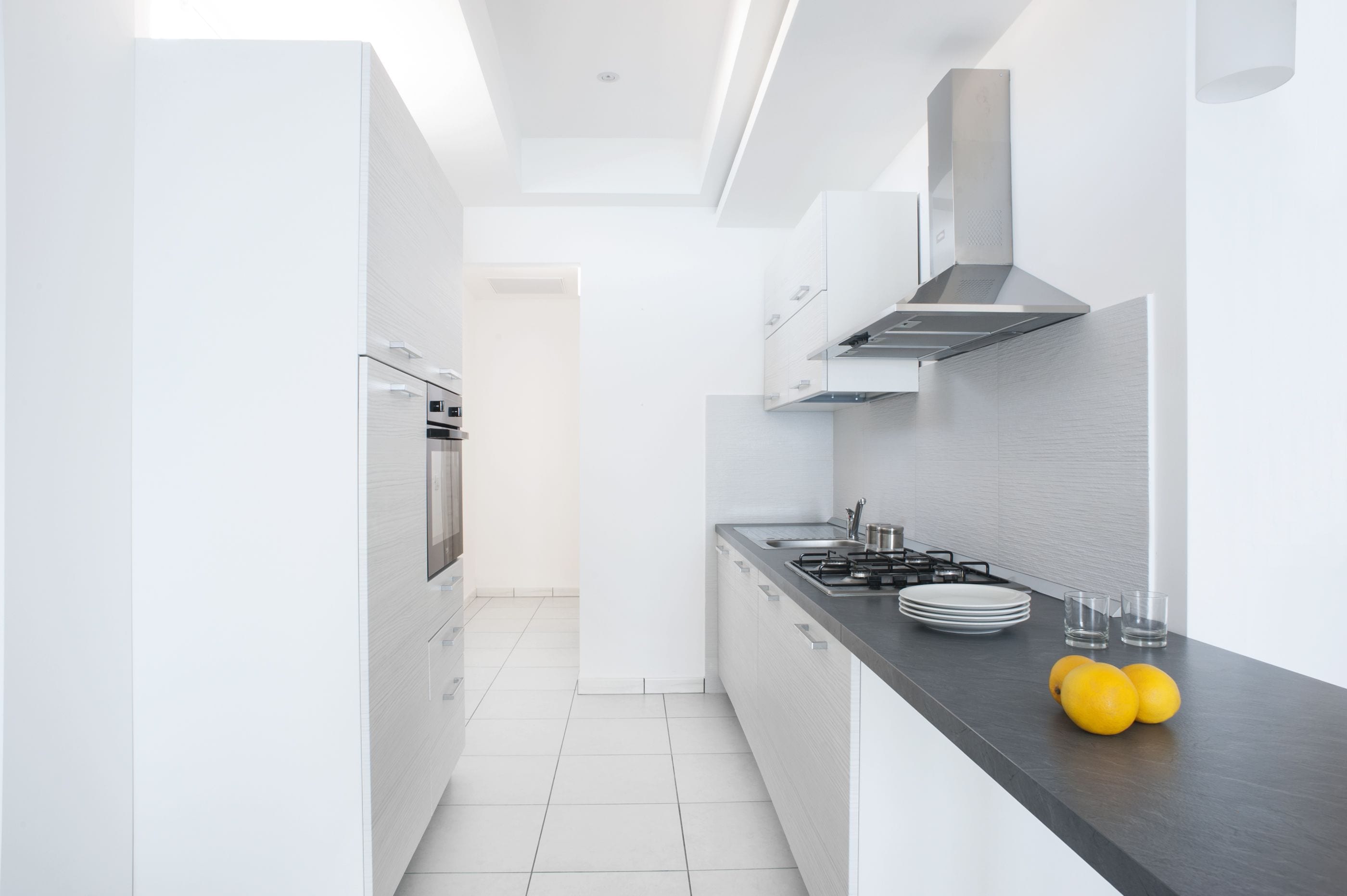 A modern kitchen with white cabinetry, a black countertop, and a stainless steel range hood.