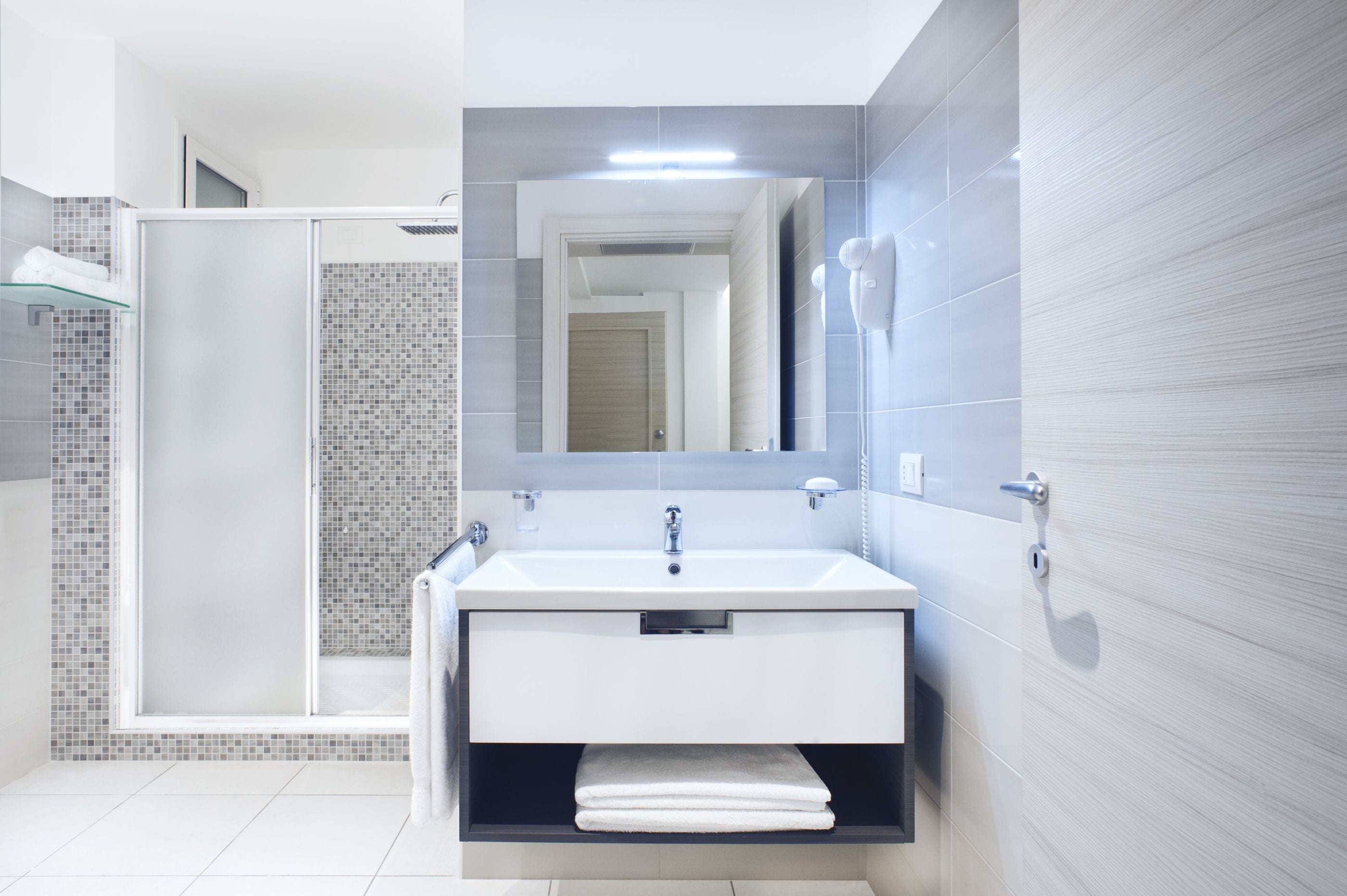 A modern bathroom with a glass-enclosed shower, a white sink, and a large mirror.