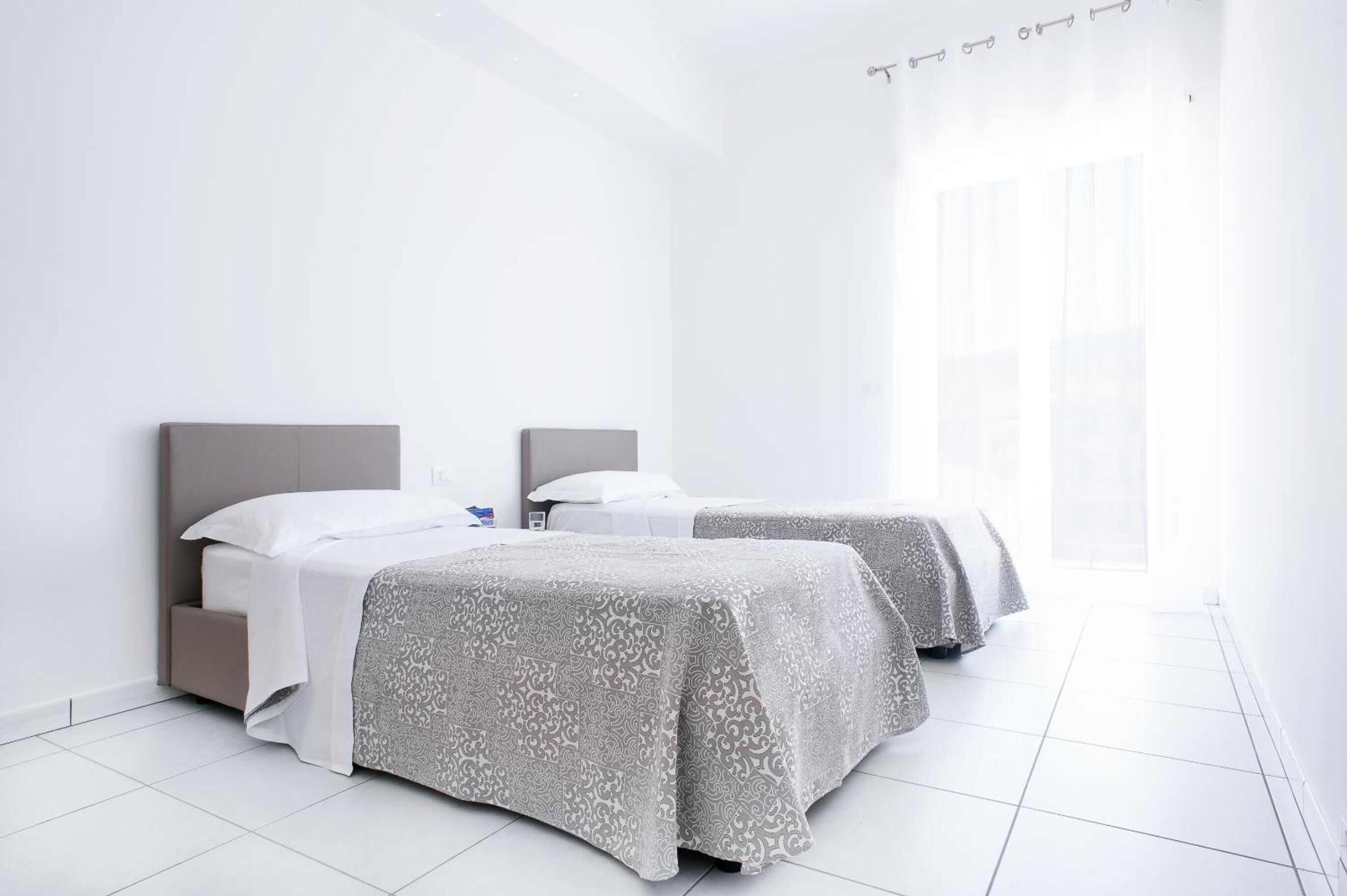 A modern hotel room with two beds, a large window, and a clean, white interior.