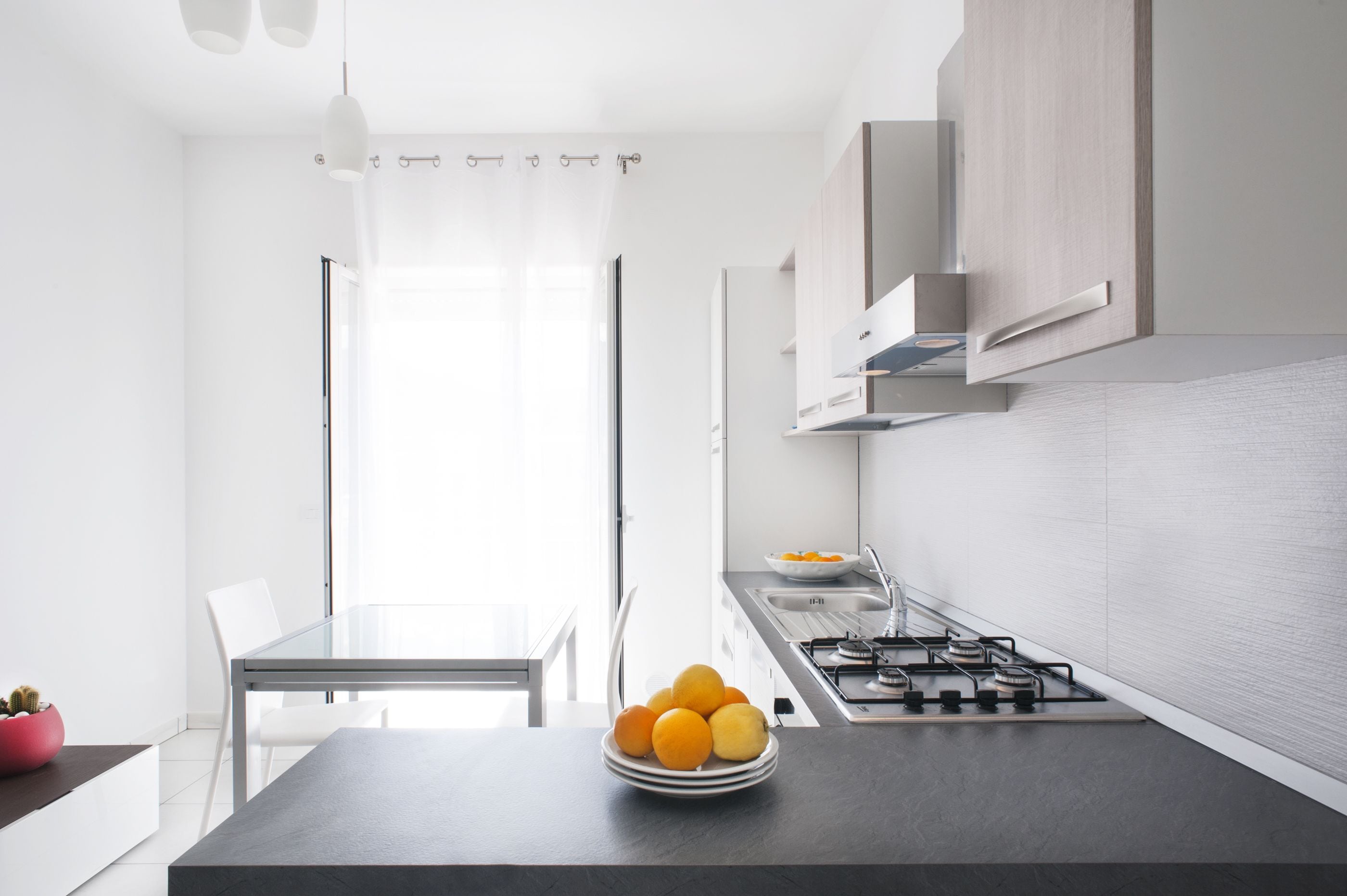 A modern kitchen with a gas stove, white cabinets, and a dining area with a glass table and chairs.