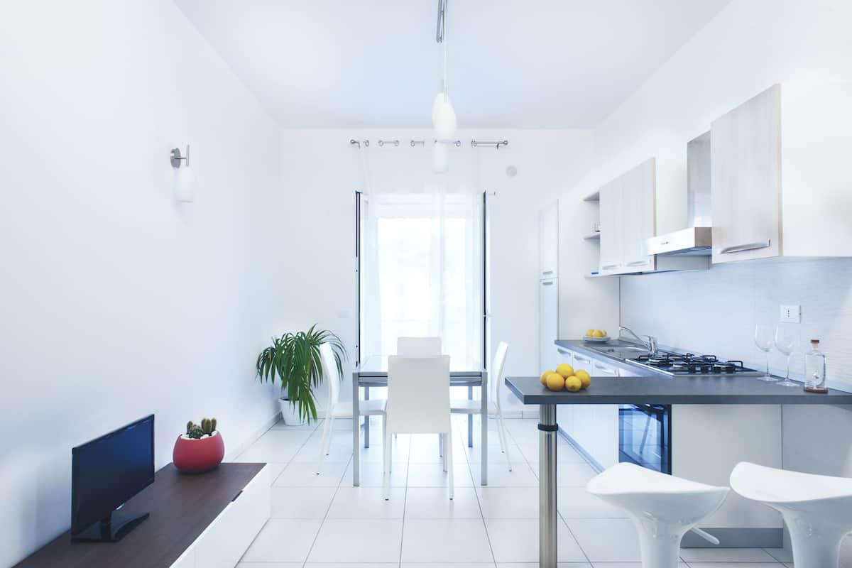 A modern kitchen with white cabinetry, a dining area with a table and chairs, and a TV on a stand.