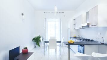 Een moderne keuken met witte kasten, een eethoek met tafel en stoelen, en een televisie op een dressoir.