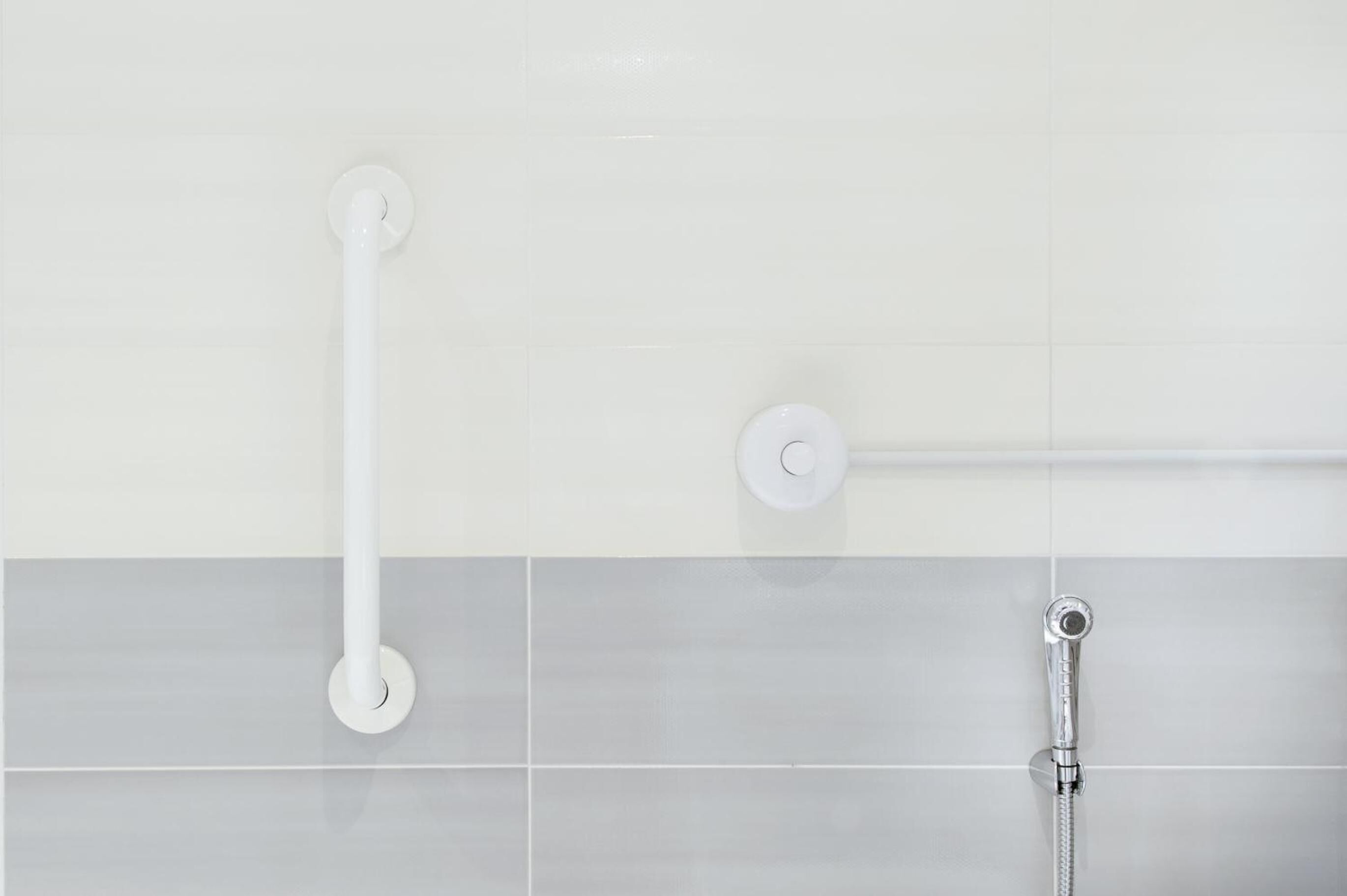 A bathroom with white tiles, a white grab bar, and a showerhead.
